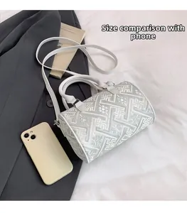 White cylinder crossbody bag with geometric embroidery shown beside phone for size comparison