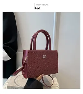 Detail of woven burgundy crossbody bag with golden hardware and letter logo