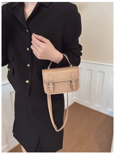 Close-up of khaki leather handbag with top handle and decorative metal buckles