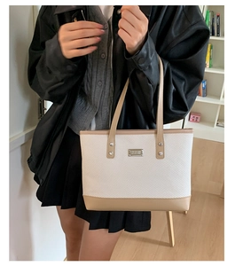 Dettaglio di una borsa tote intrecciata beige con finiture in pelle kaki e placca in metallo