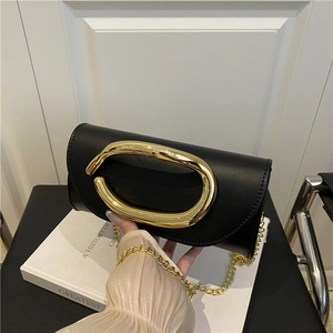 Elegant black leather evening clutch with gold oval handle and chain strap on white book