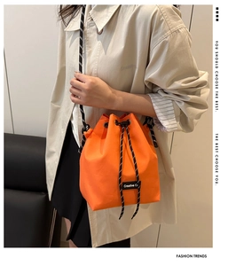 Detail view of orange nylon bucket bag featuring drawstring closure and striped strap