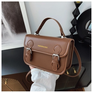 Detail of a brown vintage leather handbag showing flap closure and buckle straps in a room