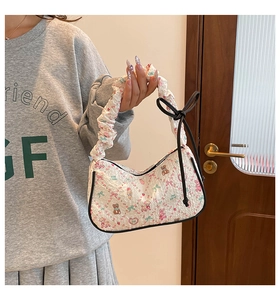 Detail of floral crescent bag with ruched handle and black bow accent on textured fabric