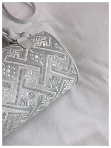 Close-up of white bucket bag featuring intricate floral embroidery and metallic silver buckle