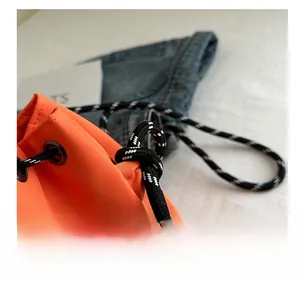Detail of bright orange nylon bucket bag with woven drawstring and metal eyelets