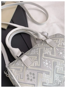 Close-up of white bucket bag with intricate floral embroidery and silver hardware