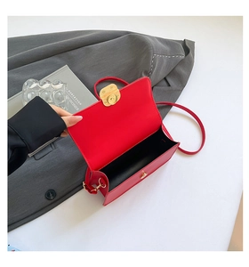 Bovenaanzicht van rode lederen tas met gouden draaisluiting op een grijze blazer