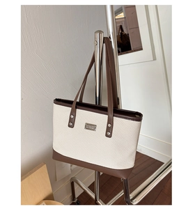 Dettaglio della borsa tote intrecciata con finiture in pelle marrone e placca in metallo