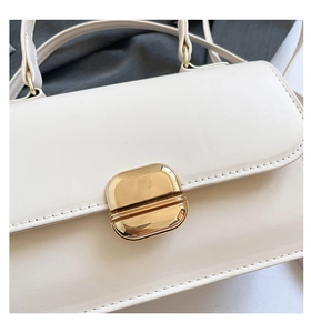 Detailed close-up of a white leather bag featuring a polished gold oval metal clasp