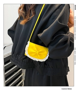Detail of a bright yellow mini crossbody bag featuring a large bow and lace trim