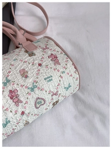 Detail of white quilted cylinder bag with cartoon prints and pink adjustable strap