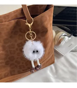Close-up of a white plush monster keychain with eyes hanging on a leopard print tote bag