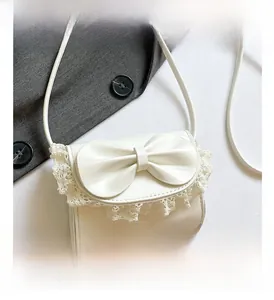 Detail shot of a cream white crossbody bag featuring a large bow and lace trim decor