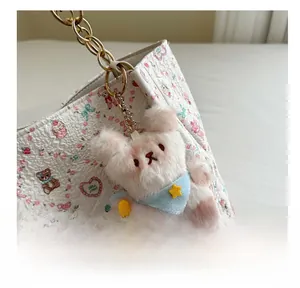 Close-up of a plush bear keychain with a blue star scarf attached to a floral handbag