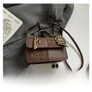 Brown leather crossbody bag with leopard print texture and silk scarf handle detail