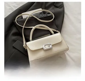 Detail of cream luxury handbag with sparkling rhinestone G-buckle on white fabric