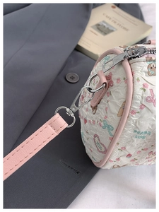 Detail of silver metal hook, pink leather strap, and bear print on pleated fabric bag