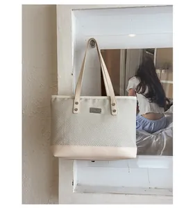 Dettaglio borsa tote intrecciata beige minimalista con finiture in similpelle e targa in metallo