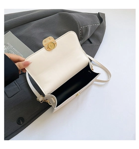 Detail van witte lederen crossbodytas met gouden gesp en zwarte voering op grijs pak