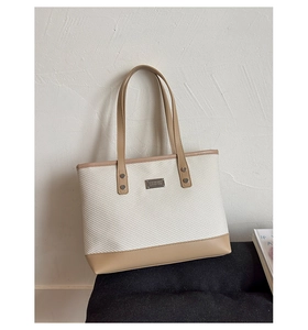 Dettaglio della borsa tote intrecciata crema con finiture in pelle e placca logo in metallo