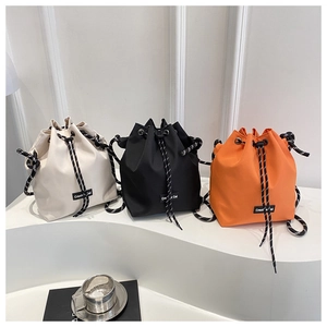 Three bucket bags in cream, black, and orange with stylish braided drawstring straps