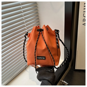 Detail of orange drawstring bucket bag featuring a woven strap and Creative Cat label