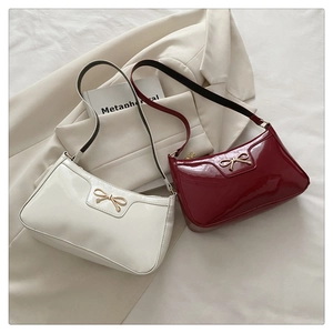Detail of elegant patent leather shoulder bags with gold bow accents in white and burgundy