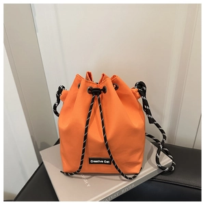 Detail view of orange nylon bucket bag with braided drawstring and leather logo patch