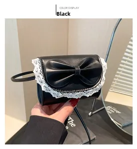 Detail of a black mini bow shoulder bag featuring white lace trim and leather texture