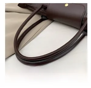 Detail of dark brown leather tote showing dual straps and gold metal hardware rings