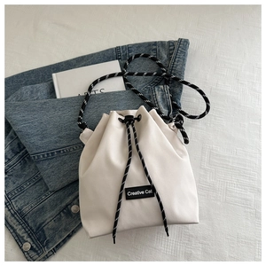 Detail view of Creative Cat white nylon bucket bag with logo patch and woven rope strap