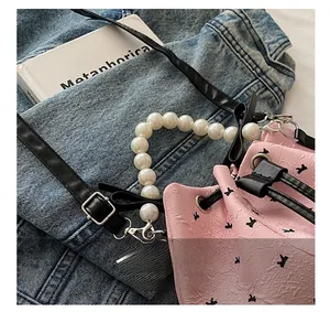 Détail d'un sac seau rose avec poignée en perles, cordon de serrage et motifs noirs