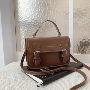 Brown vintage faux leather satchel bag with dual metal buckles on a book background