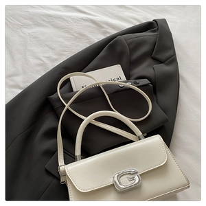 Detail of ivory leather handbag with silver G-buckle, top handle, and long shoulder strap