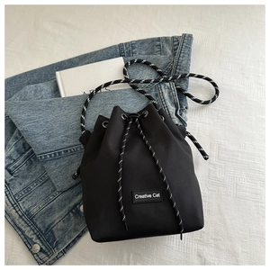 Detail of black bucket bag featuring Creative Cat logo and woven drawstring on denim