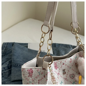 Close-up of a white textured tote bag with pink bear patterns and a rabbit plush charm
