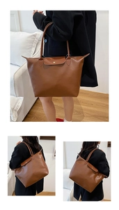 Detail view of large brown tote bag with metal snap flap and sturdy shoulder straps
