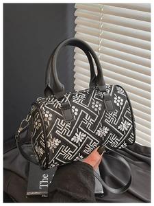 Detail of black cylinder bucket bag featuring white embroidery and metal strap buckle