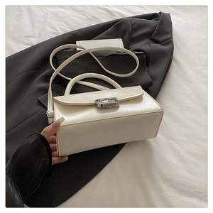 Detailed view of cream leather flap handbag with gold metal G buckle on dark background