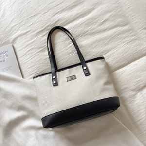 Grande borsa tote beige e nera a contrasto con manici in pelle e logo metallico