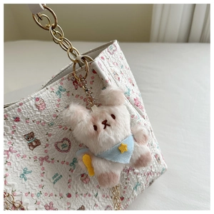 Close-up of cute white plush bear pendant with blue scarf on a white chain tote bag