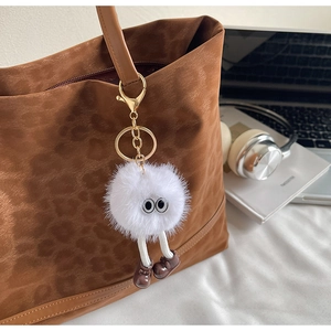 Close-up of fluffy white bag charm with big eyes and tiny shoes on a leopard print tote