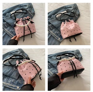Vue détaillée du sac seau rose avec nœuds noirs, poignée en perles et cordon de serrage