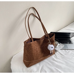 Detail of leopard print tote bag with plush charm and long shoulder straps on desk