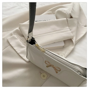Dettaglio borsa baguette bianca con fiocco dorato e tirazip a forma di fiore unico