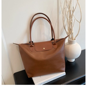 Close-up of brown leather tote bag with flap and metal snap button on a book