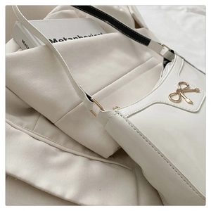 Dettaglio borsa sottobraccio in pelle verniciata bianca con fiocco dorato e trama elegante