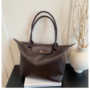 Detail of dark brown leather tote bag showing handle texture and metal snap closure