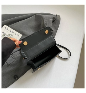 Detail shot of black leather handbag featuring dual golden magnetic snaps and spacious interior